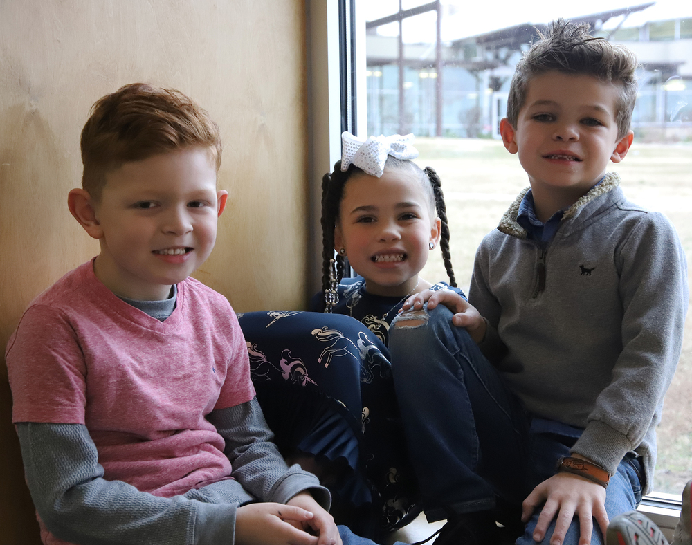 Three Fayetteville Public Schools kindergarten students posting in a window bay with bright smiles.