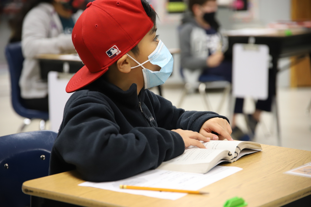 Elementary student  with mask listens intently to his teacher.